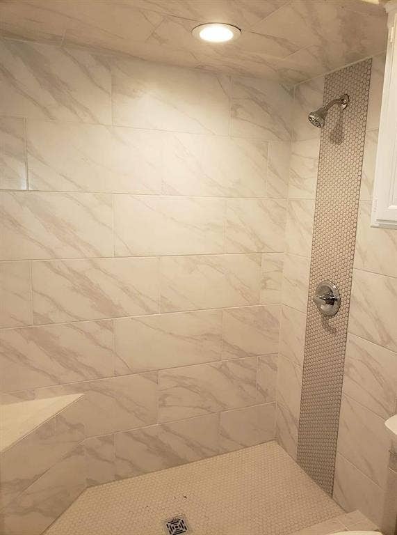 Tiled shower featuring rectangular wall tiles with subtle veining, a hexagon tile floor, a built-in corner bench, and a vertical hexagon tile accent strip
