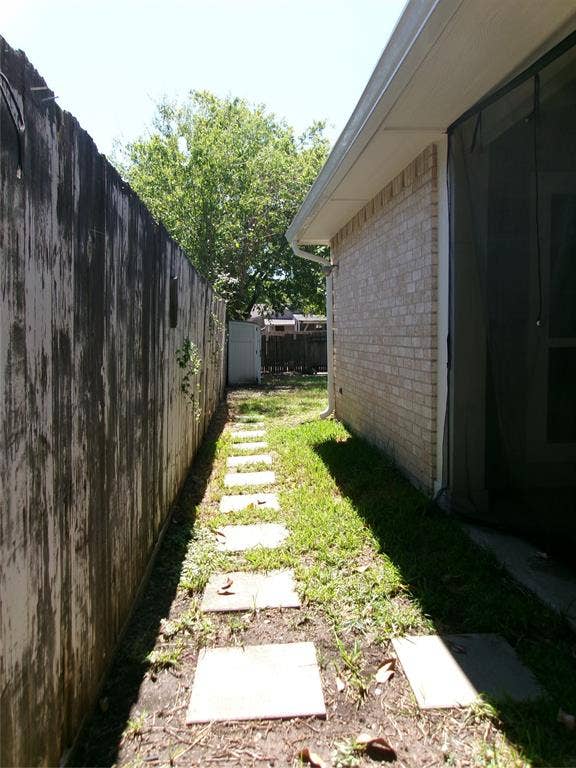 665 Stonewall Drive, Grand Prairie, TX 75052 Brick exterior with a screened enclosure, concrete stepping stone pathway, and wood fencing