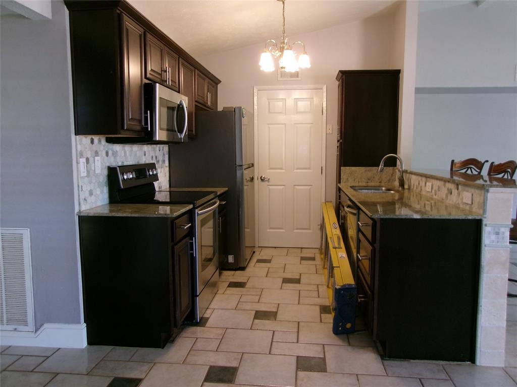 665 Stonewall Drive, Grand Prairie, TX 75052 Kitchen featuring dark wood-finish cabinetry, stainless steel appliances, mosaic tile backsplash, and light-toned countertops