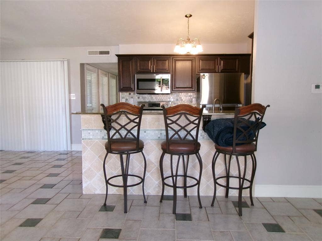 665 Stonewall Drive, Grand Prairie, TX 75052 Kitchen featuring dark wood-finish cabinetry, stainless steel appliances, a tiled backsplash, and an island with a breakfast bar