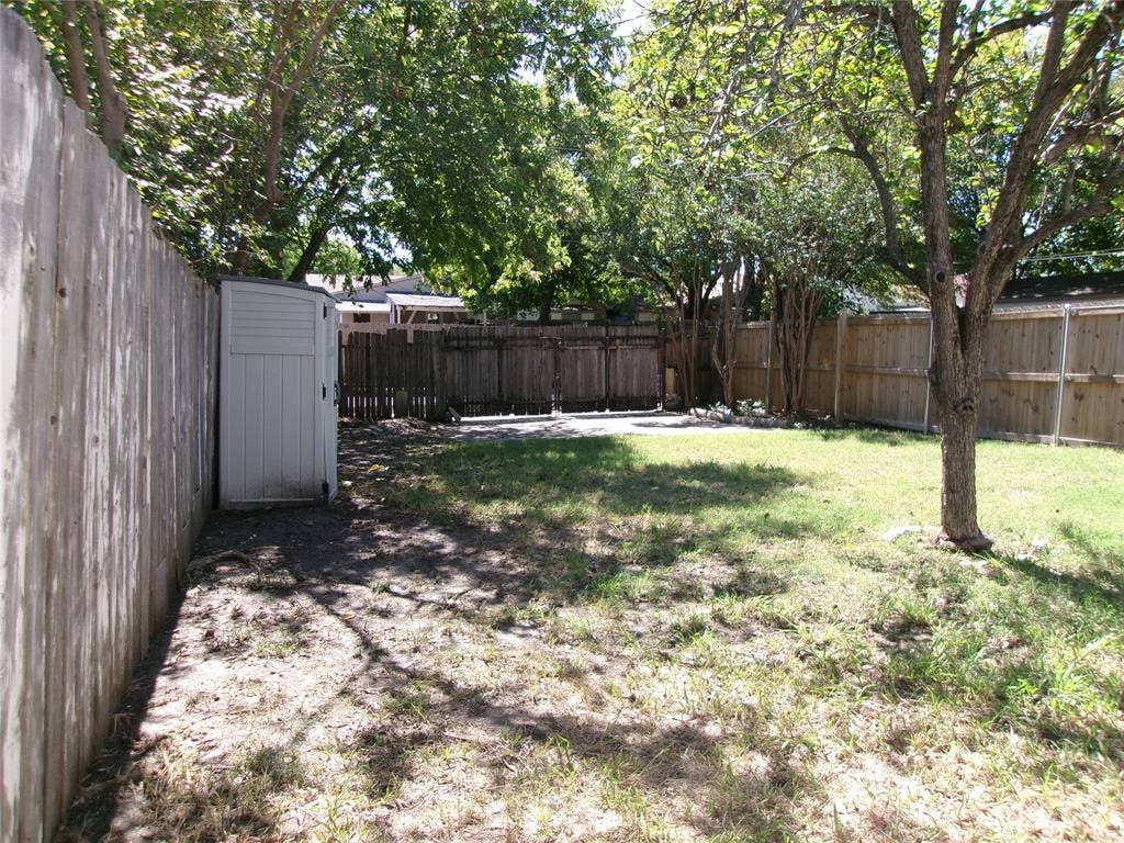 665 Stonewall Drive, Grand Prairie, TX 75052 Fenced backyard featuring a storage shed, mature trees, and a grass area