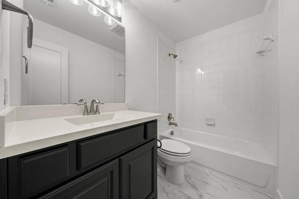 2628 Camden Court, Celina, TX 75009 Dark-toned vanity with a solid-surface countertop, rectangular integrated sink, white tile shower surround, and patterned flooring