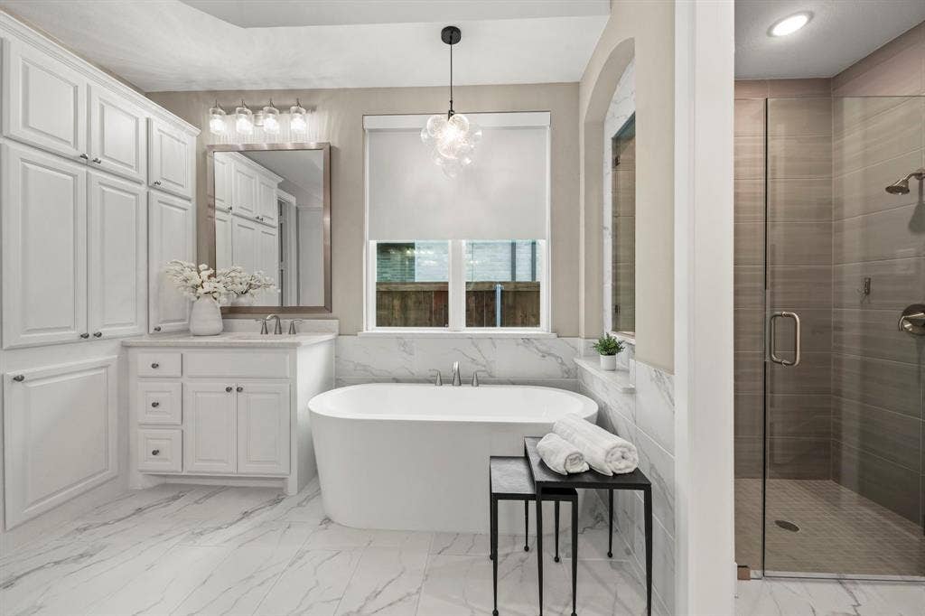 2628 Camden Court, Celina, TX 75009 Freestanding soaking tub with stone-finish surround, white cabinetry, large-format tile flooring, and walk-in shower with glass enclosure