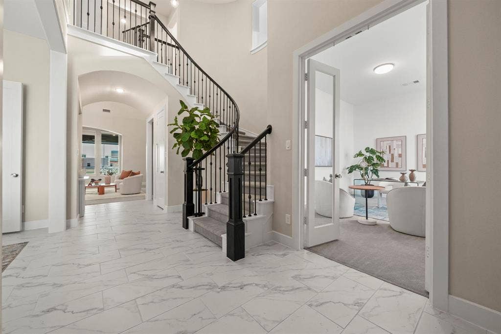 2628 Camden Court, Celina, TX 75009 Grand foyer featuring large-format tile flooring, a curved staircase with wrought-iron balusters, an arched hallway, and a glass-paned French door entry to an auxiliary room