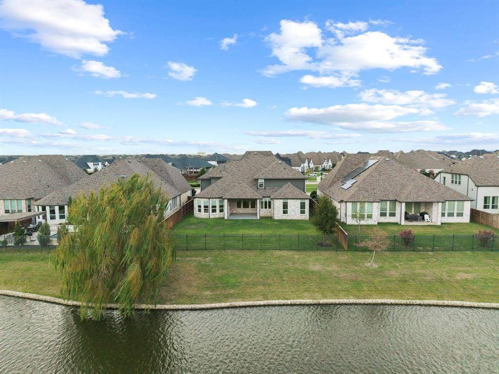 2628 Camden Court, Celina, TX 75009 Multi-gabled masonry exterior with a covered rear patio, positioned on a waterfront lot featuring a fenced backyard and a mature weeping willow