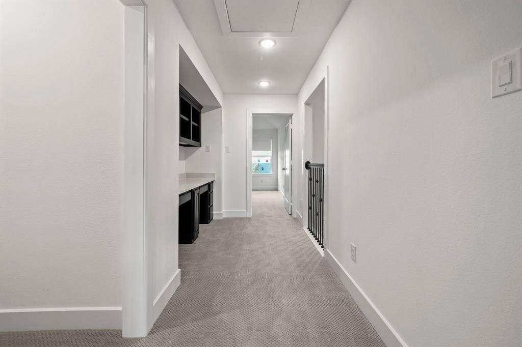 2628 Camden Court, Celina, TX 75009 Hallway featuring wall-to-wall carpeting, built-in desk with dark cabinetry and stone-surface countertop, overhead recessed lighting, and metal stair railing