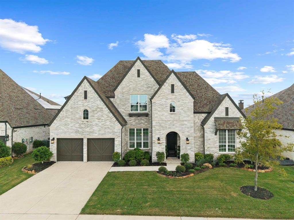2628 Camden Court, Celina, TX 75009 Stone and brick facade featuring multi-gabled rooflines, arched entryway, dark wood-finish garage doors, and manicured front landscaping