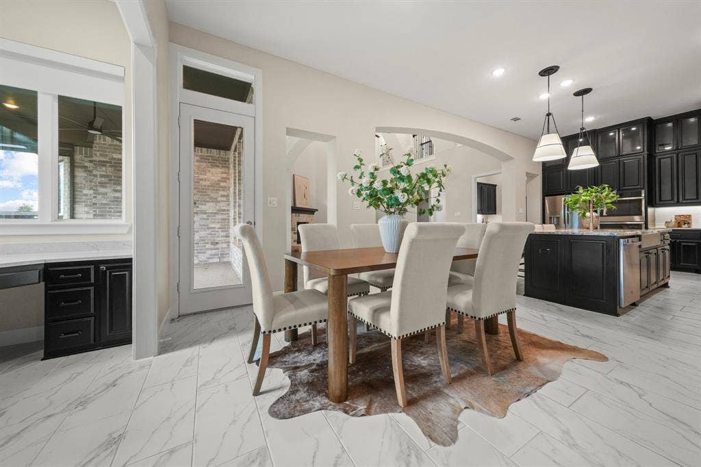 2628 Camden Court, Celina, TX 75009 Open-concept kitchen and dining area featuring stone-look tile flooring, shaker-style cabinetry, a central island with an integrated sink, dual pendant lighting, and arched architectural details