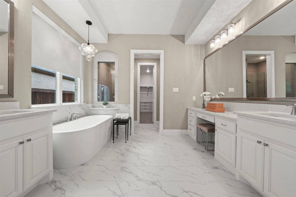 2628 Camden Court, Celina, TX 75009 Bathroom featuring dual white vanities with stone-surface countertops, a freestanding soaking tub, large-format tile flooring, and a recessed vanity area