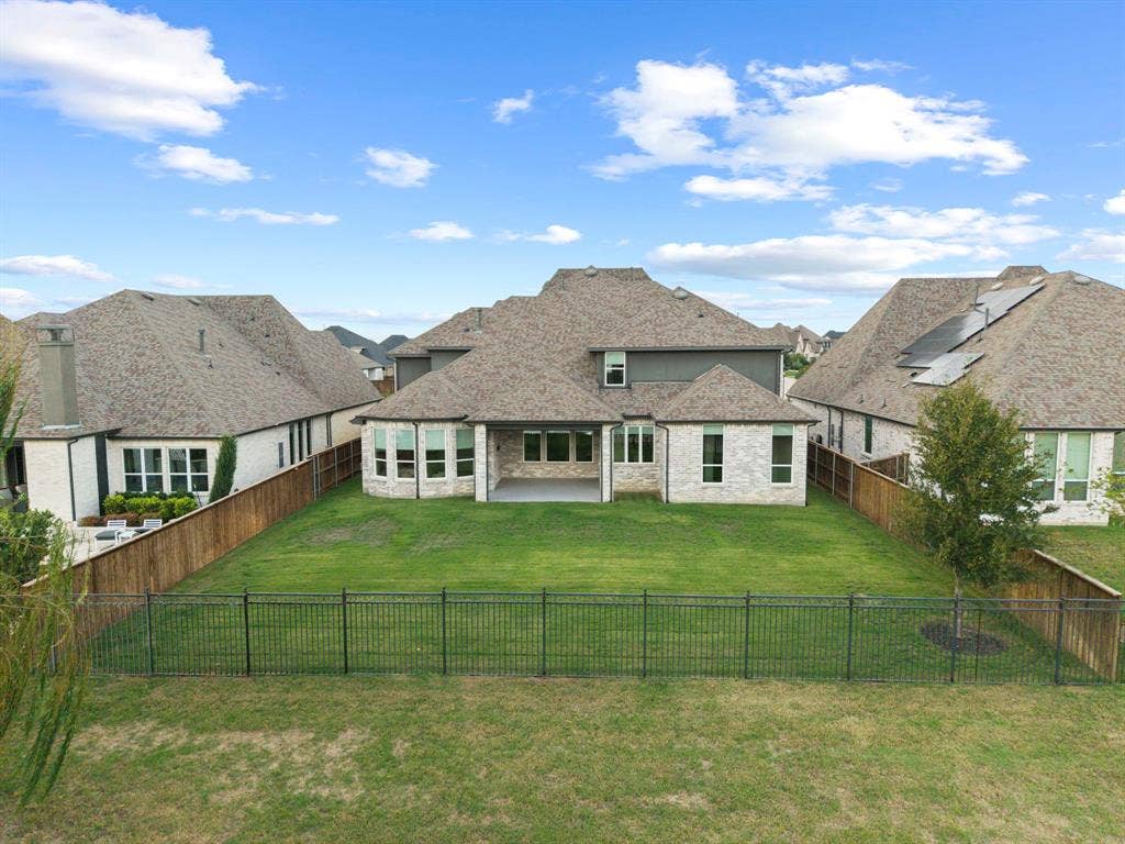 2628 Camden Court, Celina, TX 75009 Rear exterior featuring light-toned masonry, a covered patio, multiple multi-pane windows, a fenced backyard, and a composition shingle roof