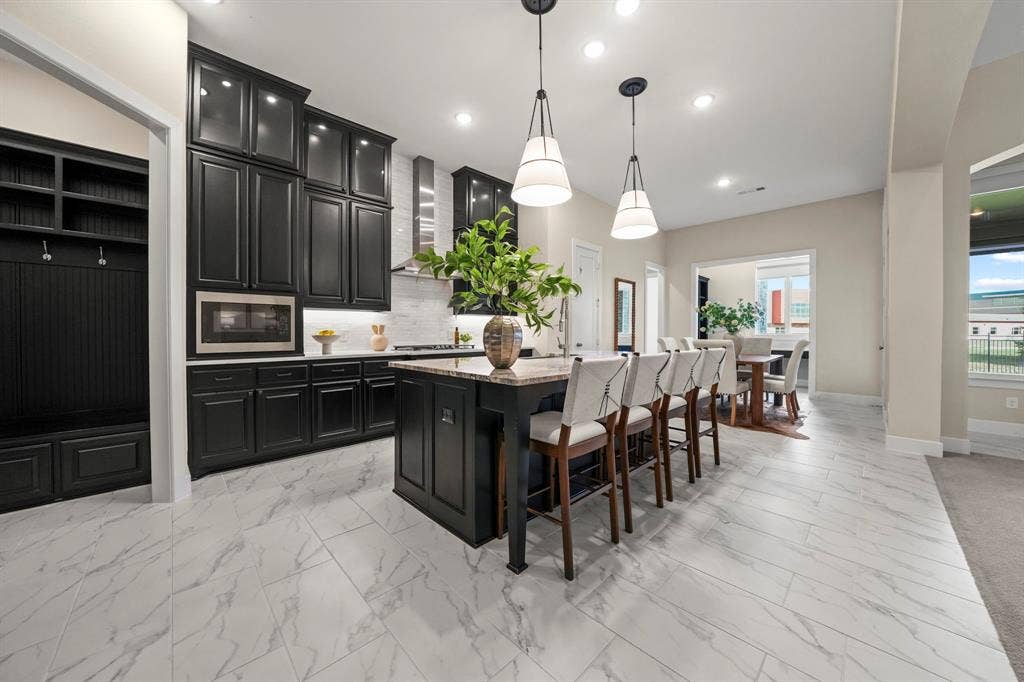 2628 Camden Court, Celina, TX 75009 Kitchen featuring floor-to-ceiling dark cabinetry, stone-finish countertops, a central island, patterned tile flooring, and built-in mudroom storage