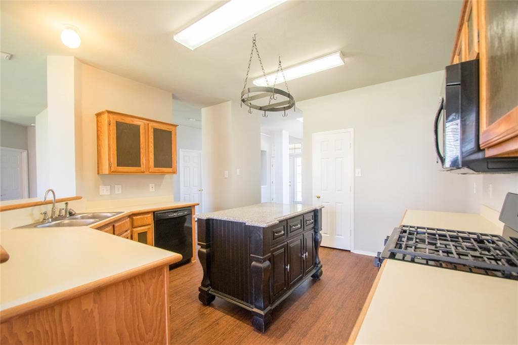 Kitchen featuring a central island with a granite-look countertop, wood-finish flooring, light wood cabinetry, and a gas range