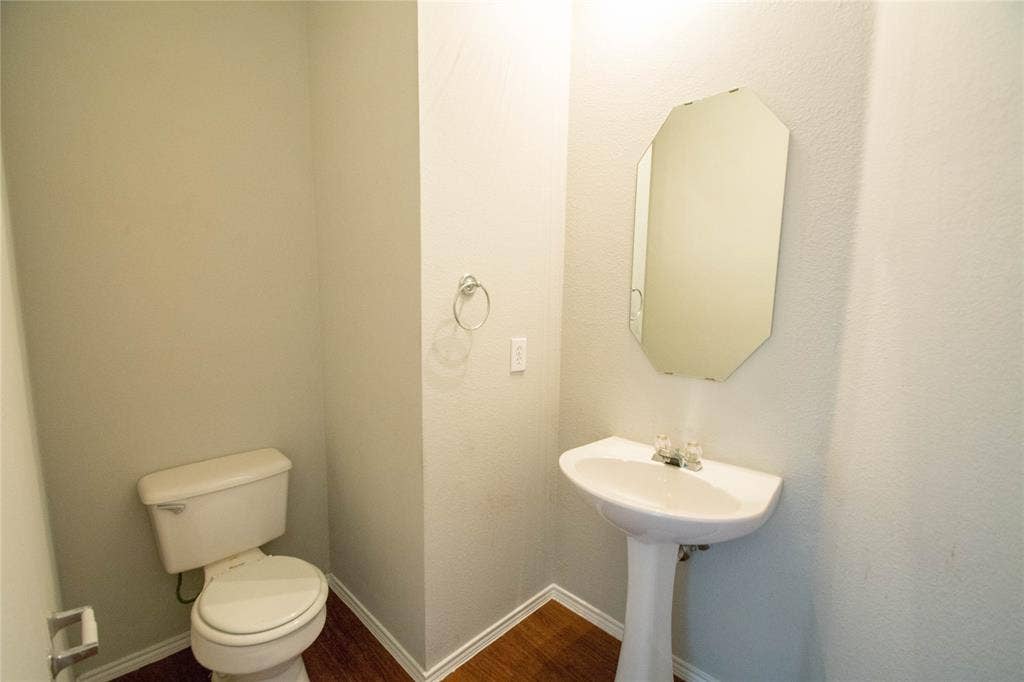 Pedestal sink with chrome fixtures, octagonal mirror, and wood-finish flooring