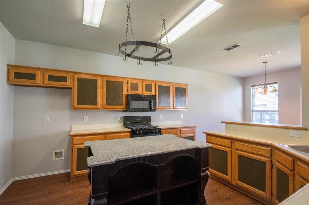 Kitchen featuring wood cabinetry, stone countertops, a central island with a granite surface, and wood-finish flooring