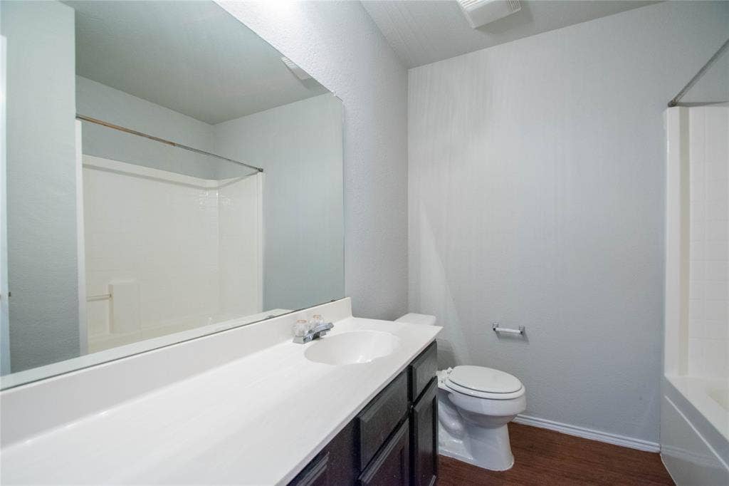Bathroom featuring a single vanity with an integrated sink, dark wood-finish cabinetry, a large wall-mounted mirror, and wood-look flooring