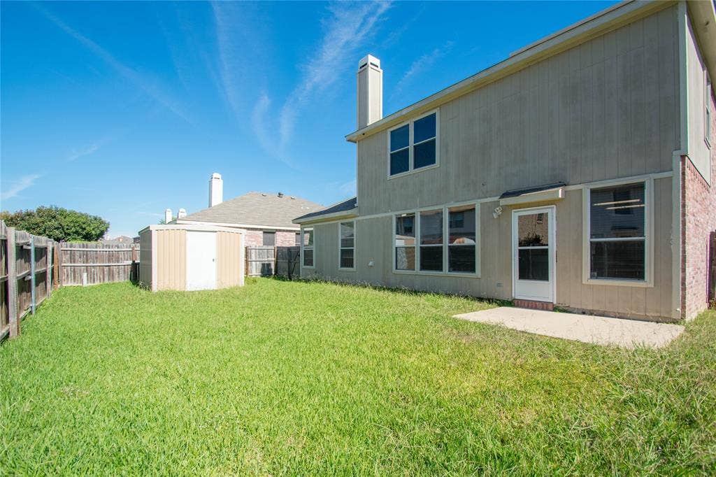 Expansive grassy yard featuring a wood privacy fence, a storage shed, and a concrete patio