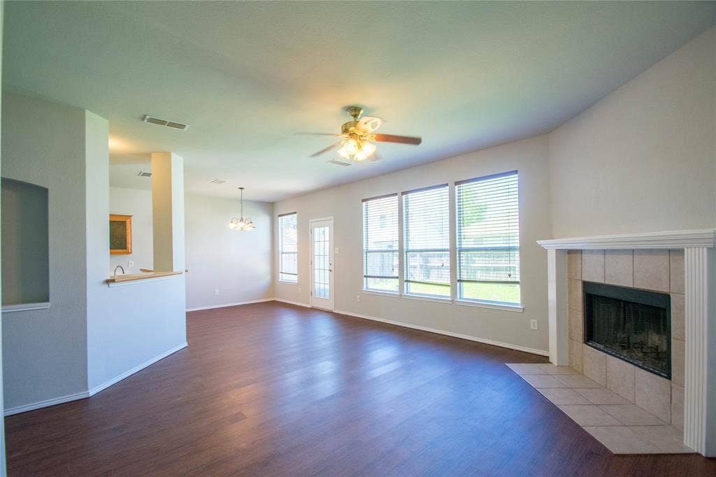 Spacious interior with wood-finish flooring, a ceiling fan, a fireplace with a tiled surround and mantel, and multiple windows