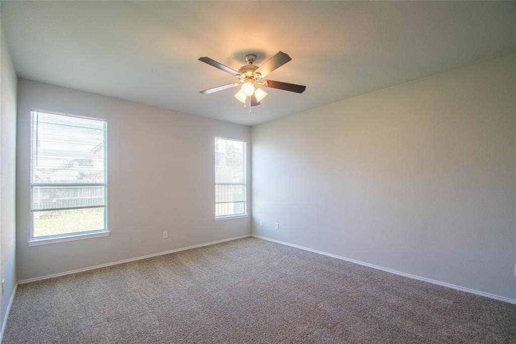 Spacious room with neutral-toned carpet, two windows with blinds, and a ceiling fan with integrated lighting
