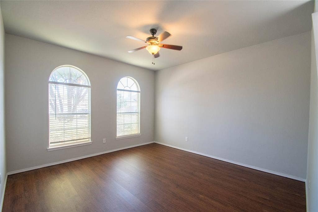 Wood-finish flooring, two arched windows with blinds, and a ceiling fan with integrated lighting