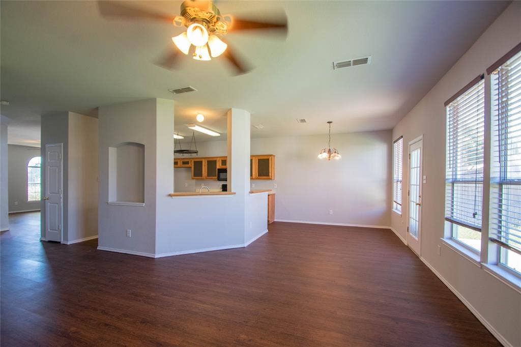 Spacious room featuring wood-finish flooring, a ceiling fan, and multiple windows with blinds
