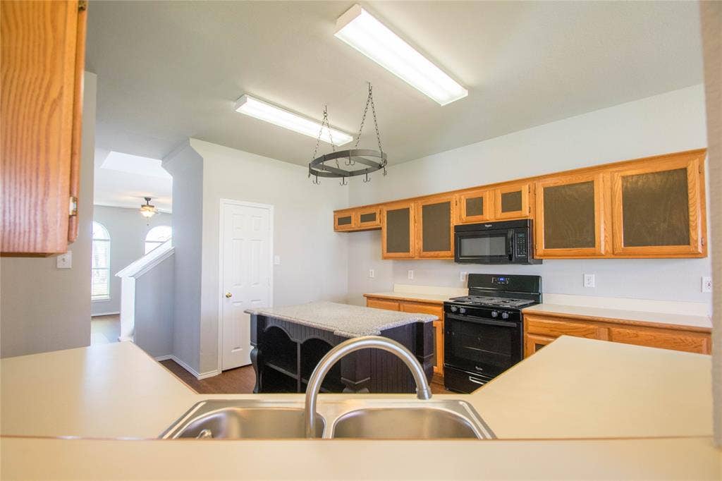 Kitchen featuring wood cabinetry, black appliances, a central island with a stone-finish countertop, and a double basin sink with a high-arc faucet