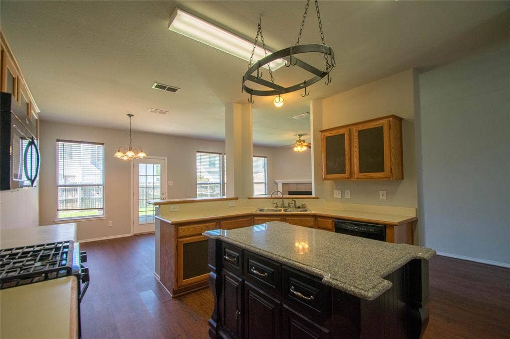 Kitchen featuring a central island with a granite countertop, wood-finish flooring, recessed lighting, built-in cabinetry, and a black appliance suite