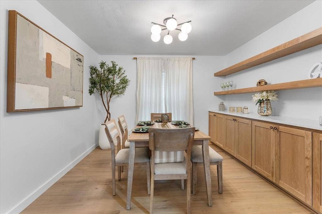 Light wood-finish flooring, built-in lower cabinetry with white countertops, two floating wood shelves, and a modern ceiling light fixture