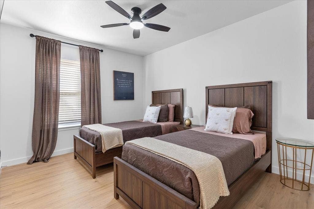 Light wood-finish flooring, a window with horizontal blinds, and a ceiling fan with integrated lighting