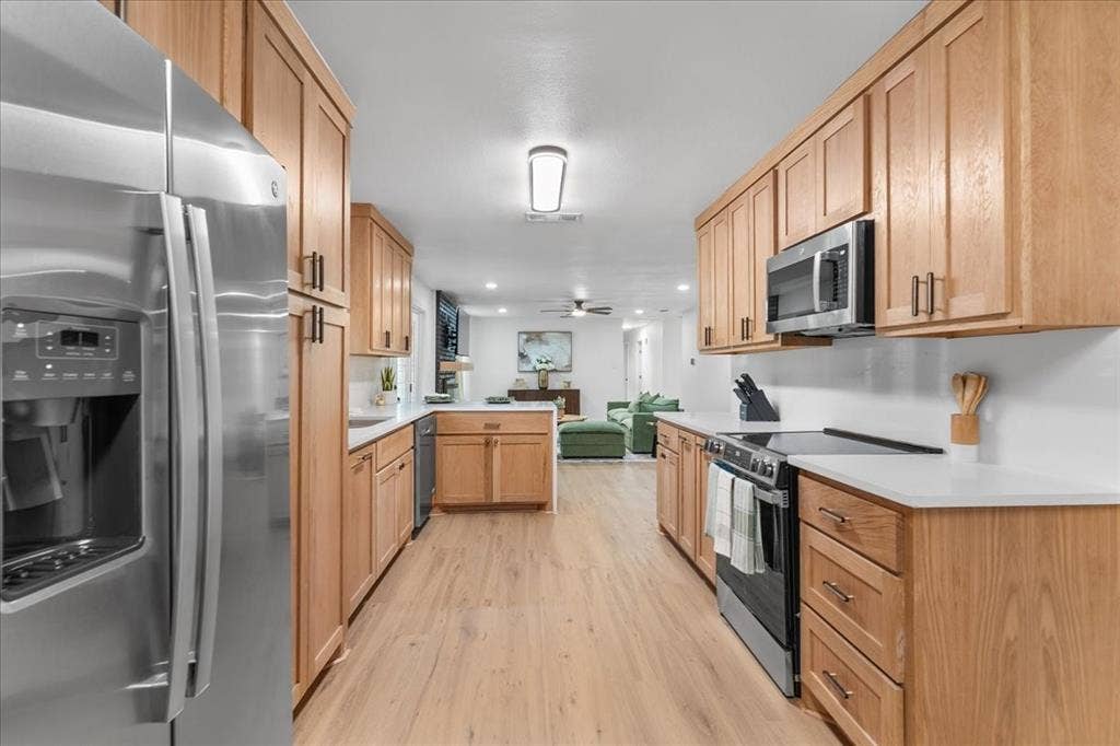 Galley kitchen featuring wood cabinetry, stainless steel appliances, white countertops, wood-finish flooring, and recessed lighting