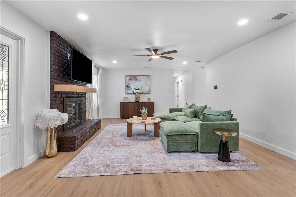 Spacious living area featuring wood-finish flooring, a dark brick fireplace with a wood mantel, recessed lighting, and a ceiling fan