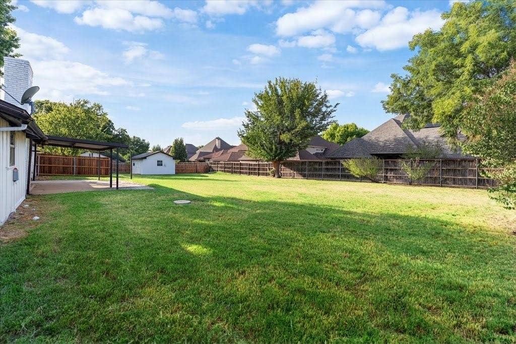 Expansive green lawn with a covered concrete patio, privacy fencing, and a detached storage shed