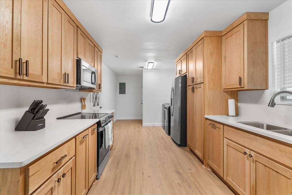 Wood-finish flooring, light wood cabinetry, white countertops, stainless steel appliances, and a double basin sink