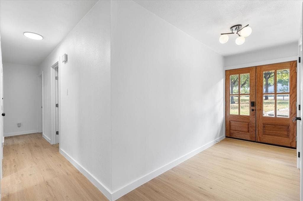 Wood-finish flooring throughout, bright white walls, modern ceiling light fixture, and wood-paneled double entry doors with glass lites