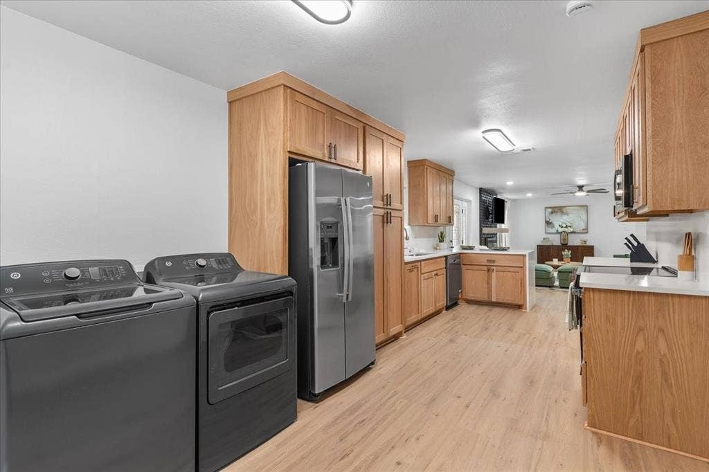 Wood-finish flooring throughout, light wood cabinetry, stainless steel refrigerator, white countertops, and white walls
