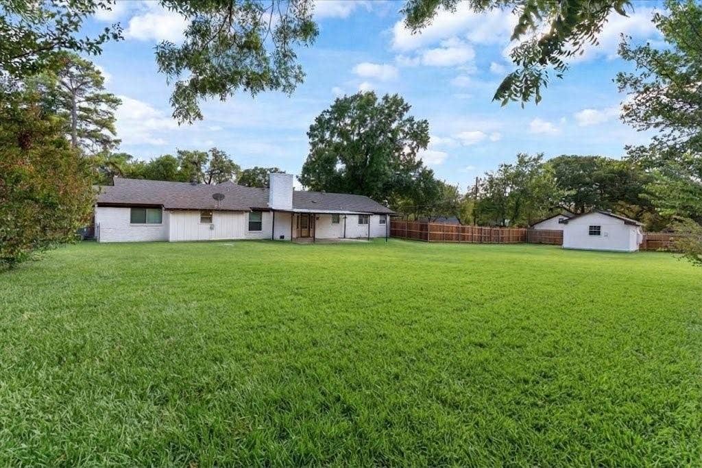 Expansive backyard featuring a manicured lawn, established trees, a covered patio, and a detached structure