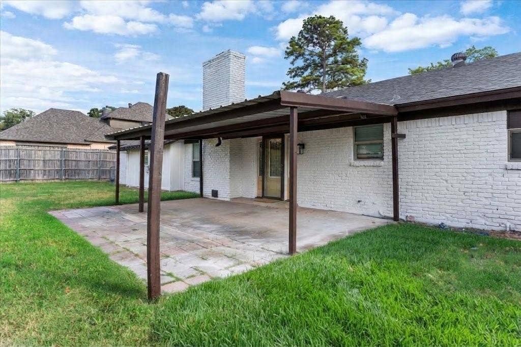 Covered patio area with concrete and paver flooring, white brick exterior, and a prominent chimney feature