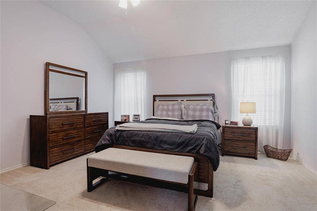 2918 Periwinkle Court, Garland, TX 75040 Vaulted ceiling, ceiling fan, two windows with white blinds, and light-toned carpet flooring