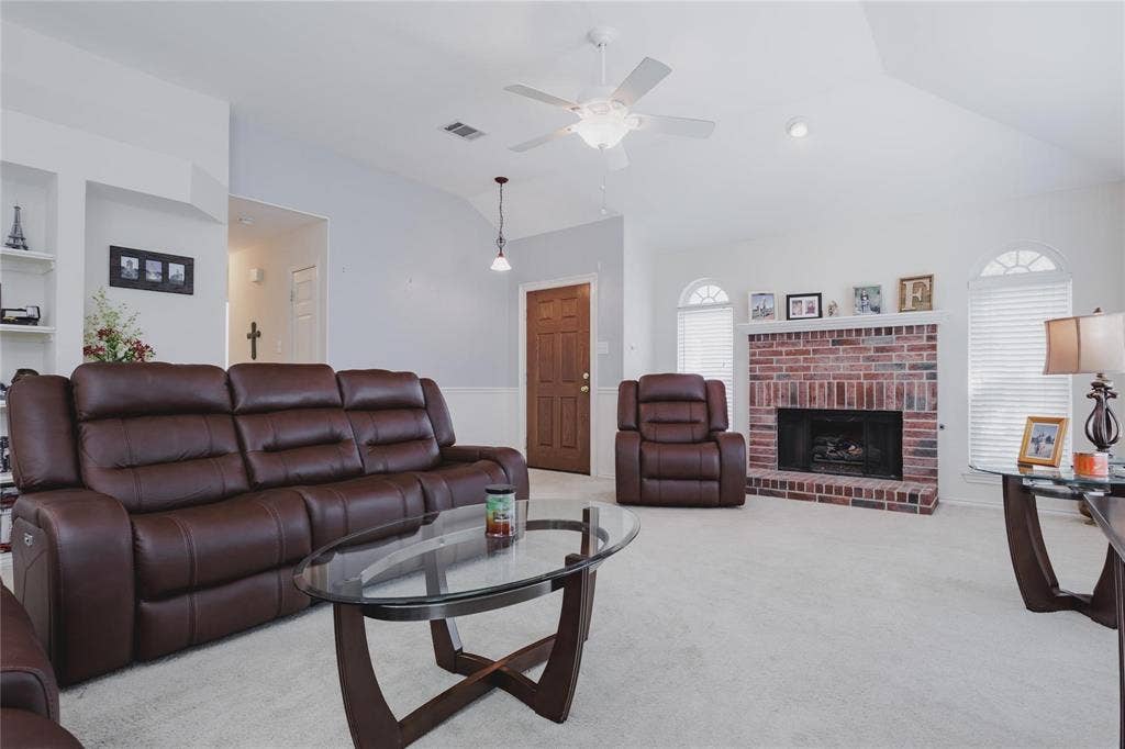 2918 Periwinkle Court, Garland, TX 75040 Vaulted ceilings, brick fireplace, built-in shelving, arched windows with blinds, and a ceiling fan with integrated lighting