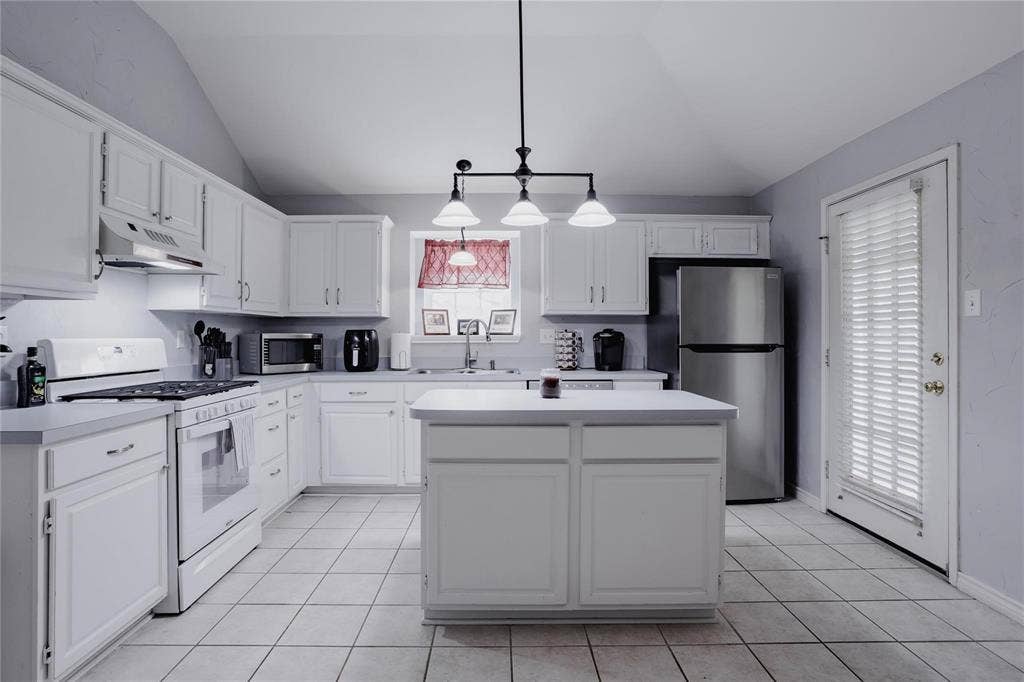 2918 Periwinkle Court, Garland, TX 75040 Kitchen featuring vaulted ceilings, white cabinetry, a central island, tile flooring, and stainless steel appliances