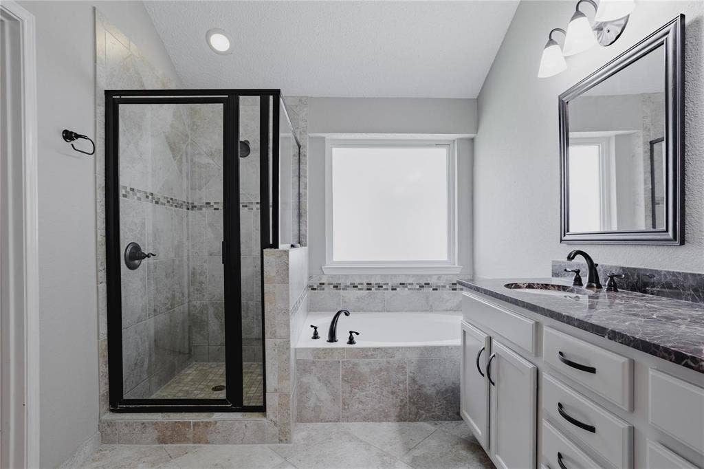 2918 Periwinkle Court, Garland, TX 75040 Walk-in shower with dark-framed glass enclosure, built-in soaking tub, vanity with stone countertop, under-mount sink, and dark-finish hardware