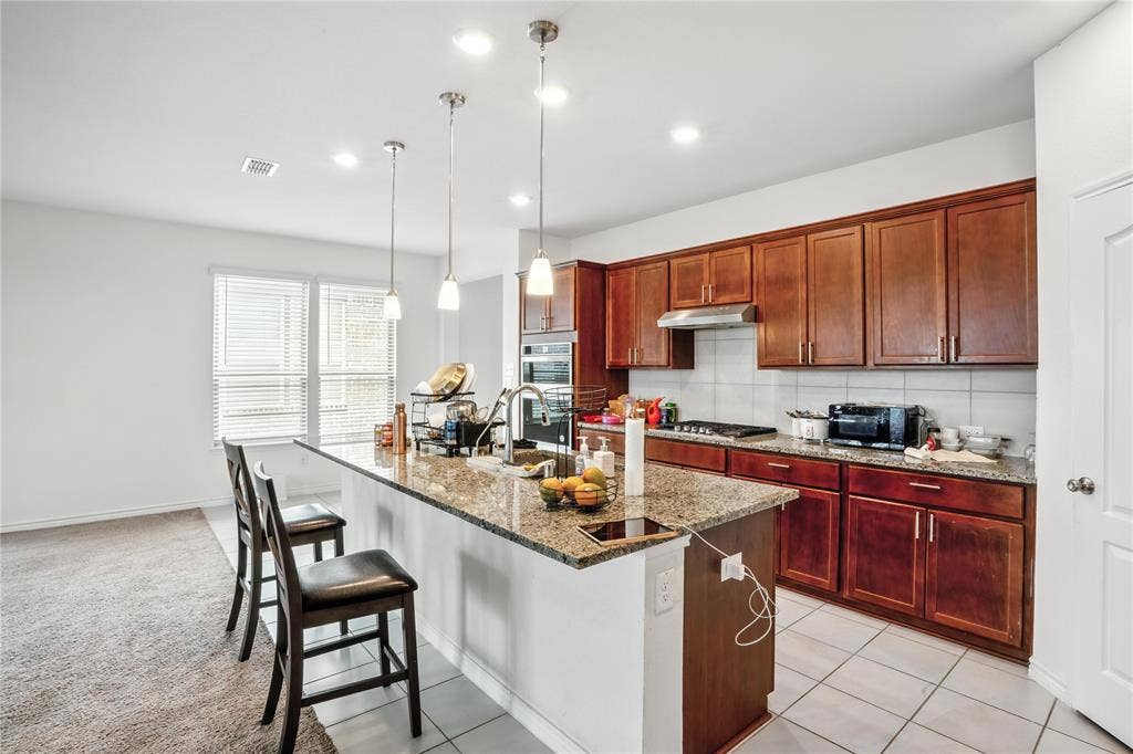 Kitchen featuring tasteful backsplash, dark brown cabinets, a kitchen breakfast bar, light stone counters, and a kitchen island with sink