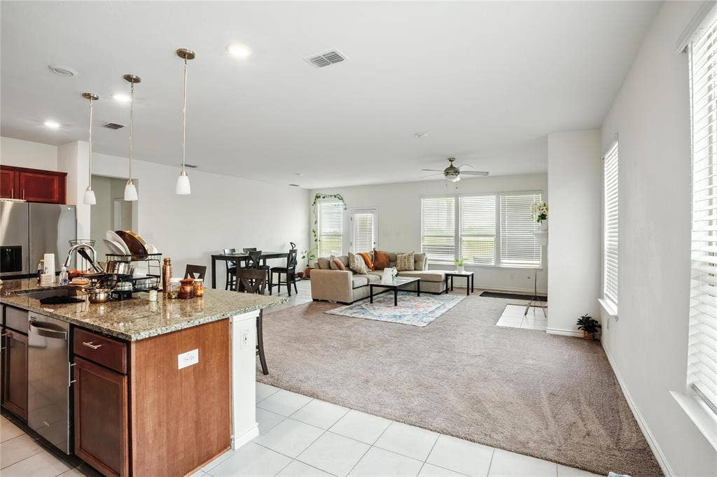 Kitchen featuring light stone counters, light tile patterned floors, light colored carpet, hanging light fixtures, and open floor plan