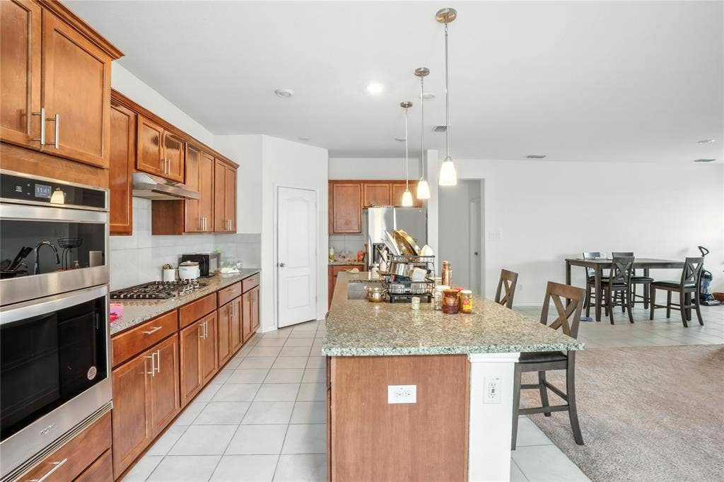 Kitchen with stainless steel appliances, light tile patterned flooring, a kitchen island, and a kitchen breakfast bar