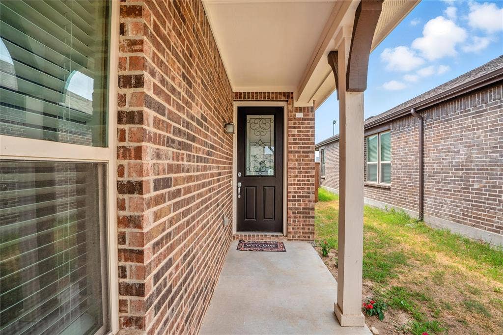 View of exterior entry with brick siding and covered porch