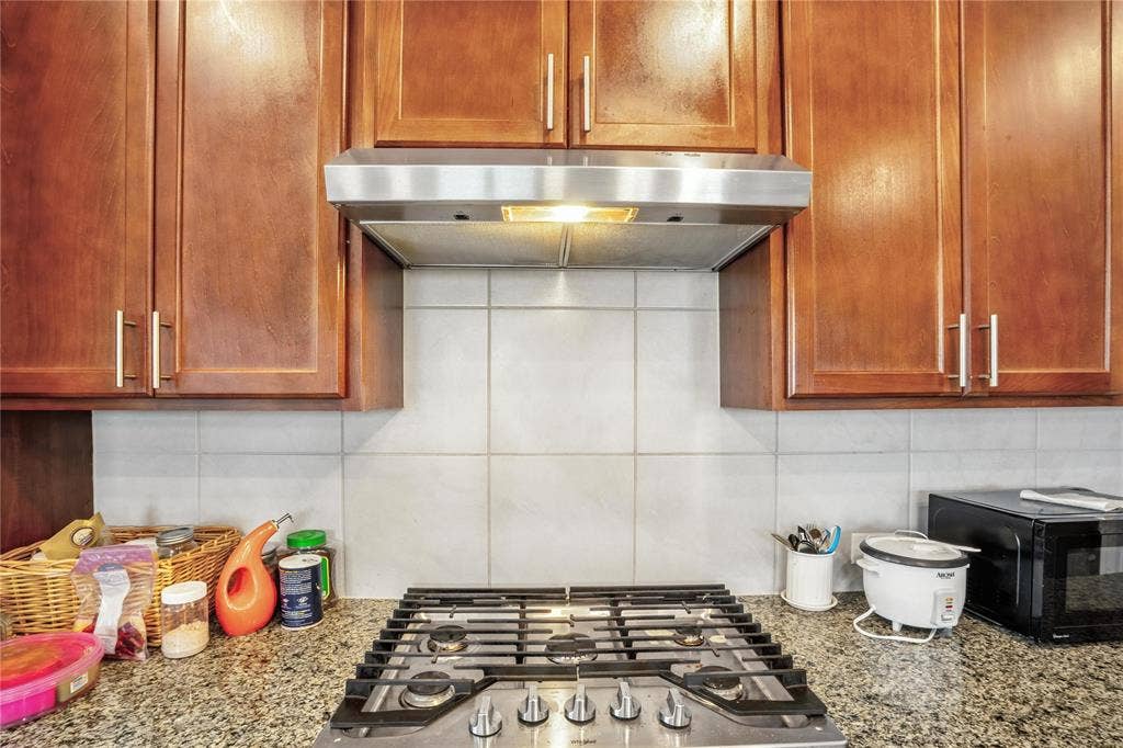 Kitchen featuring stainless steel gas stovetop, decorative backsplash, wall chimney range hood, and light stone countertops