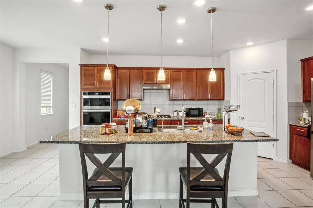 Kitchen with tasteful backsplash, a breakfast bar, stainless steel double oven, light stone counters, and recessed lighting