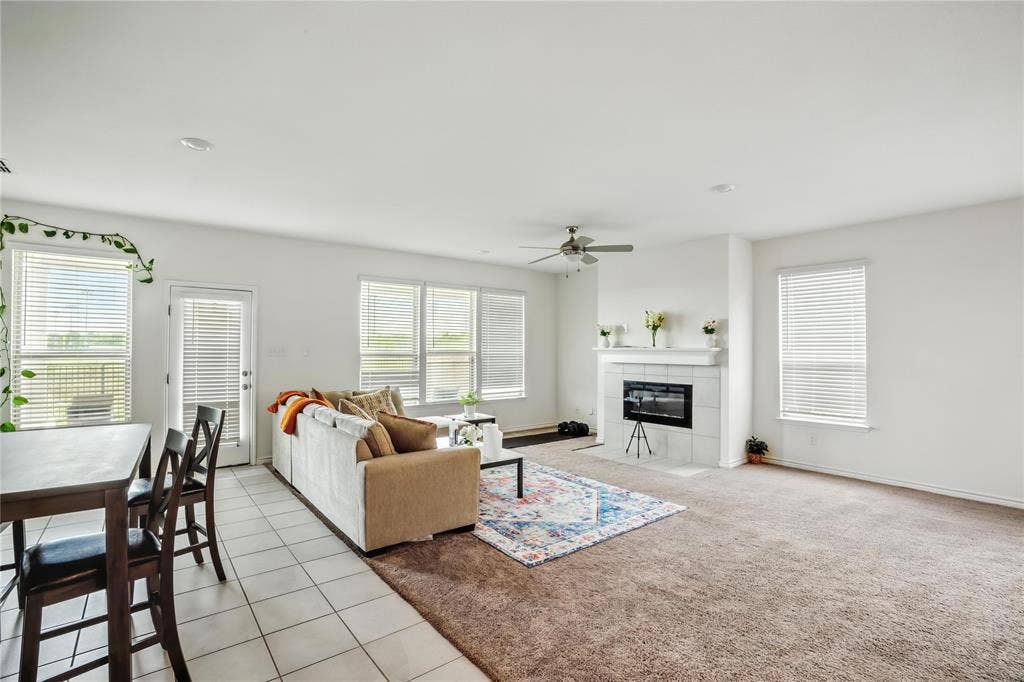 Living room with light colored carpet, a fireplace, light tile patterned flooring, and a ceiling fan