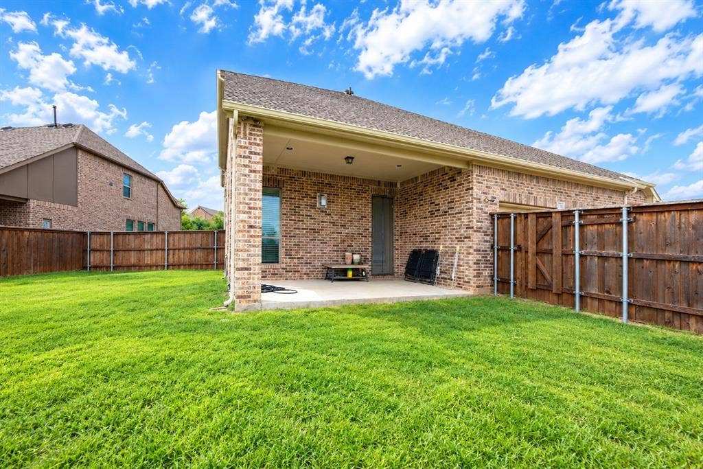 1603 Coventry Court, Farmers Branch, TX 75234 Expansive green lawn, brick exterior, covered patio, privacy fencing, and a window with dark trim