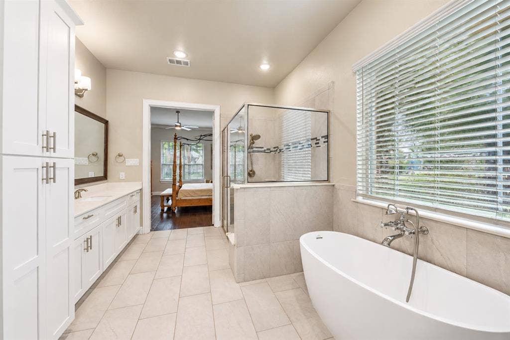 1603 Coventry Court, Farmers Branch, TX 75234 Freestanding soaking tub, walk-in shower with glass enclosure, dual vanity with white cabinetry, and large window with blinds