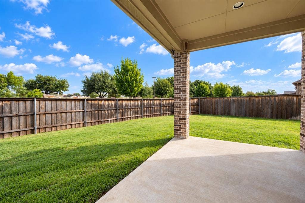 1603 Coventry Court, Farmers Branch, TX 75234 Expansive backyard featuring a manicured lawn, full privacy fencing, and a covered concrete patio with brick columns